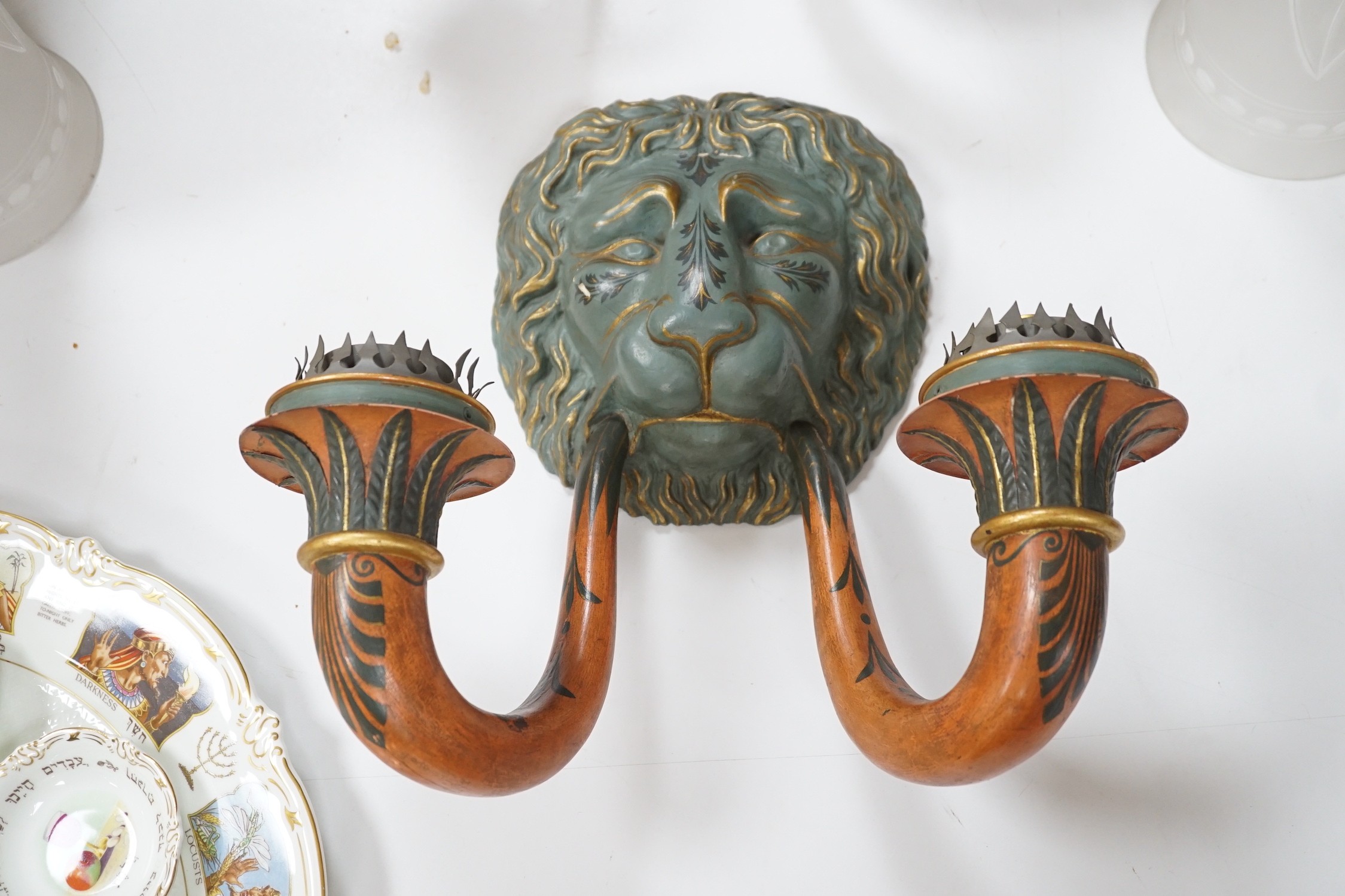 A pair of carved and decoratively painted twin-branch lion mask wall lights with tall glass shades, wall lights 38cms high, shades 32cms high
